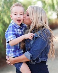 a woman kisses her son in front of a tree